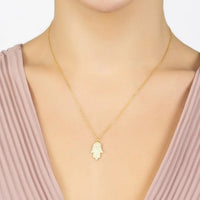 Gold-tone hamsa pendant necklace with small hand-shaped charm worn at neckline