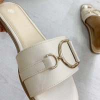 Cream slide sandals with wide strap and gold-tone ring buckle detail, close-up