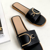 Black slide sandals with wide strap and gold-tone ring buckle detail, pair view