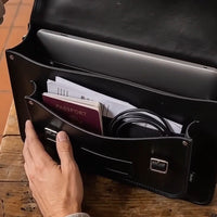Black leather satchel open top showing documents inside and a pen holder pocket.