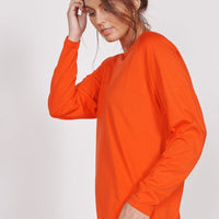 Orange long-sleeve training top, side view with draped hem and relaxed fit