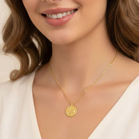 Gold-tone necklace with round Leo zodiac pendant, worn on V-neck white top