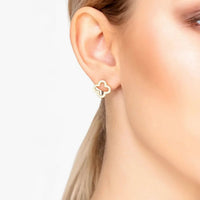 Gold clover stud earrings on a woman's ear
