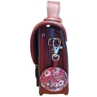 Oxblood leather satchel side view with adjustable strap and floral-lined round pocket