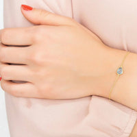 Gold bracelet with blue teardrop stone on wrist, thin linked chain