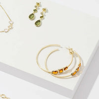 Gold-tone hoop earrings featuring green teardrop gemstones and small round stones