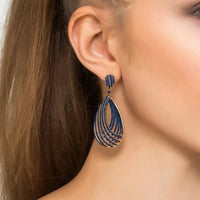 Gold-tone sapphire blue CZ teardrop hoop earrings worn on ear