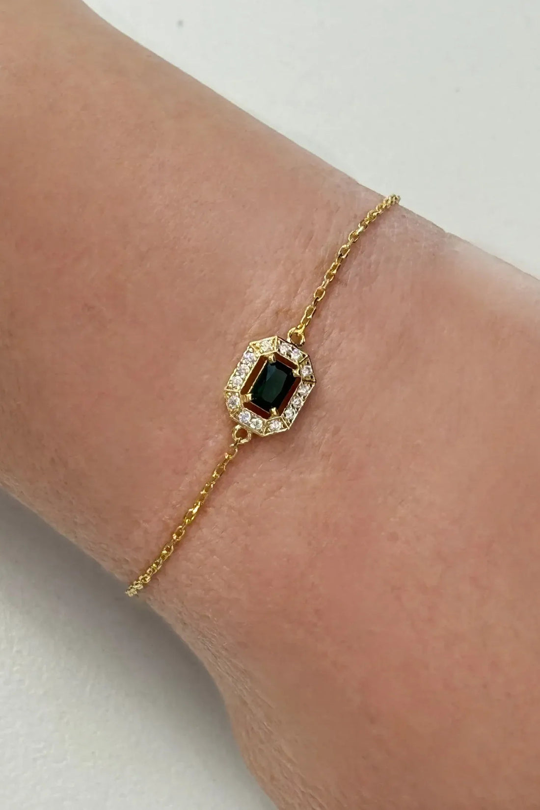 Gold gemstone bracelet with emerald green stone in ornate rectangular frame