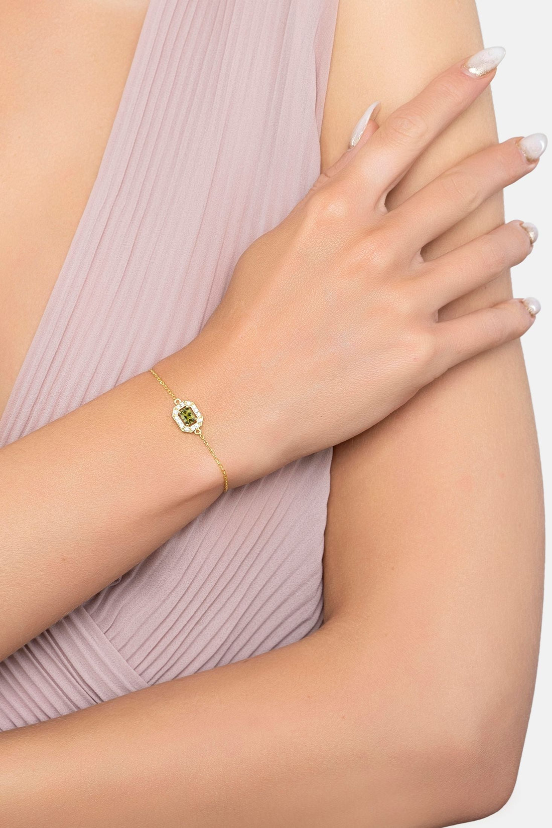 Gold gemstone bracelet on wrist with green square center stone and slim chain