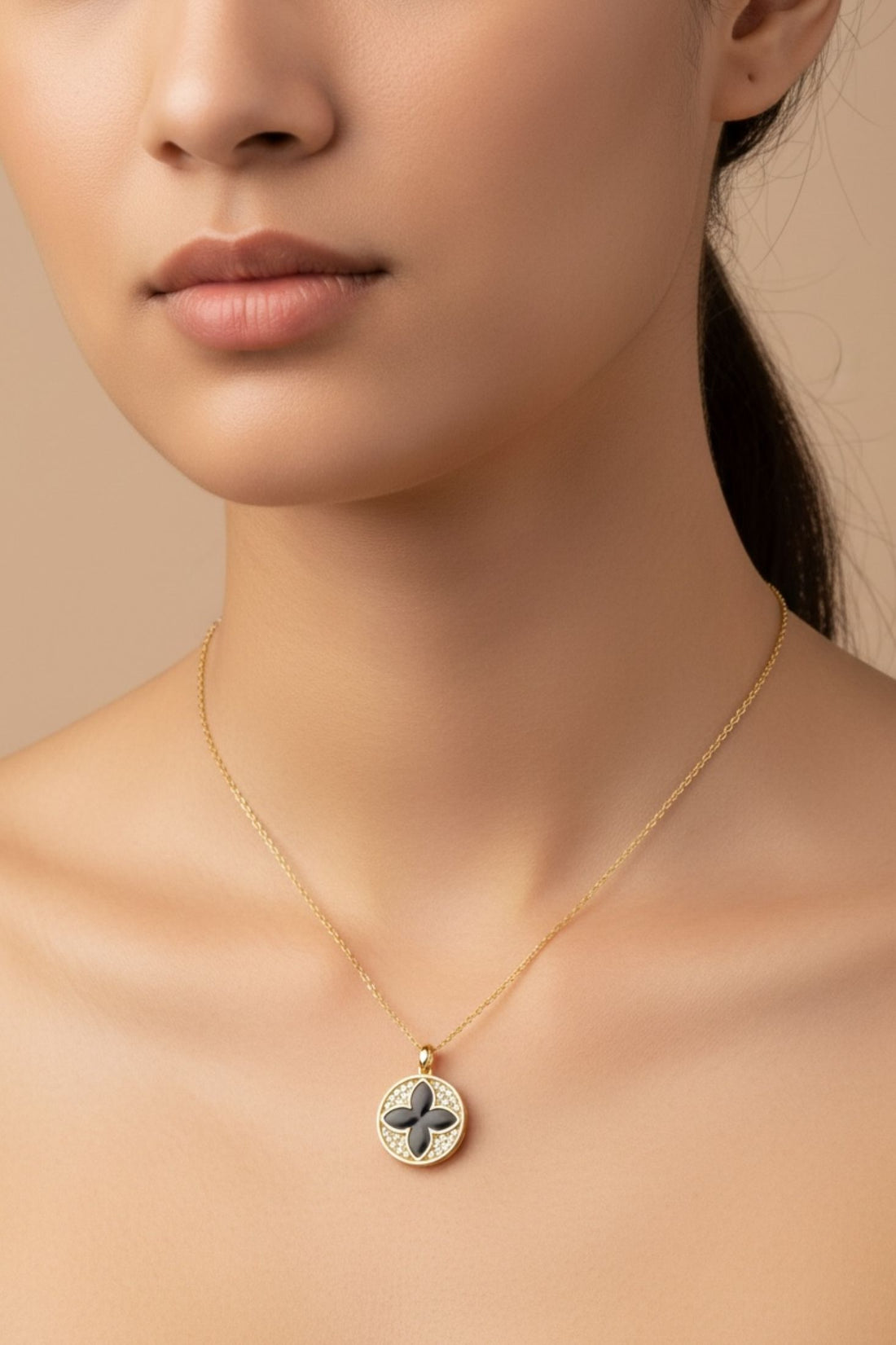 Gold necklace close-up: round clover pendant with black enamel center on chain