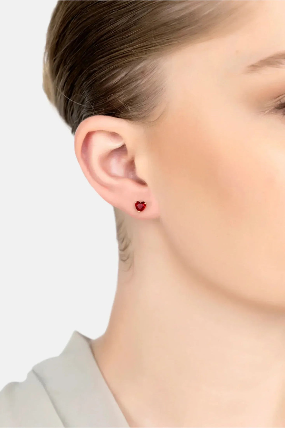 Red ruby heart stud earring on gold post, worn on ear