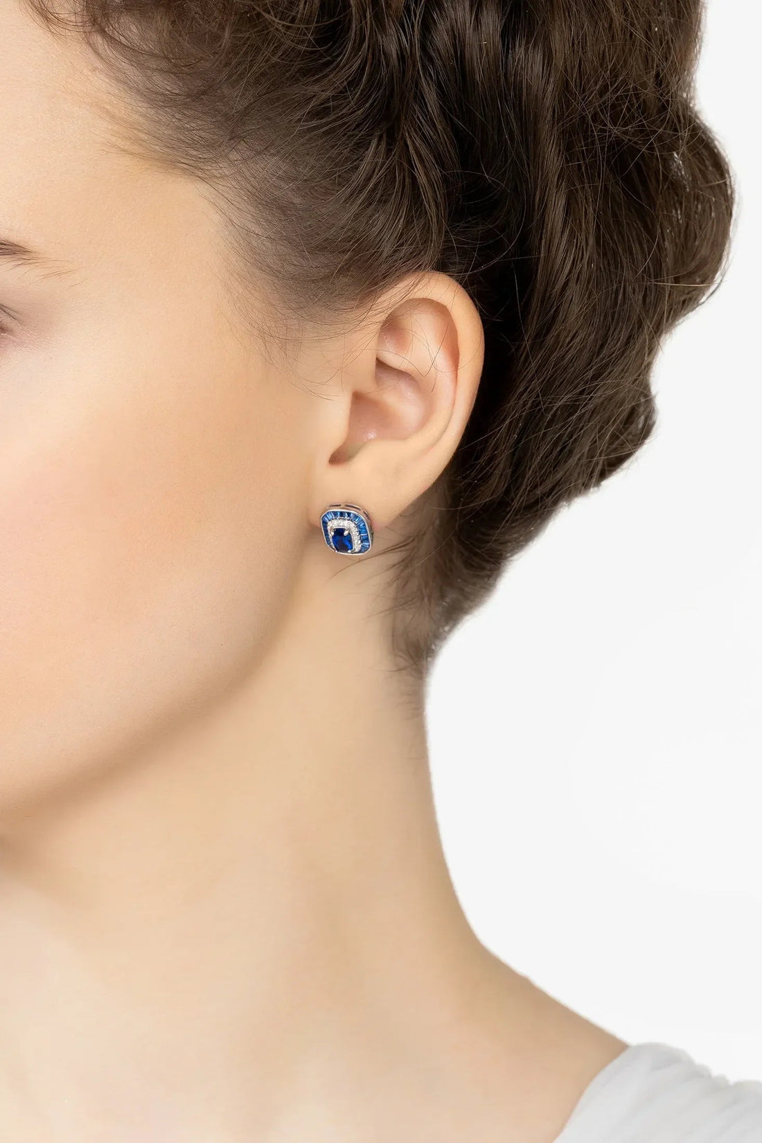 Blue sapphire stud earrings on ear with silver setting and crystal border