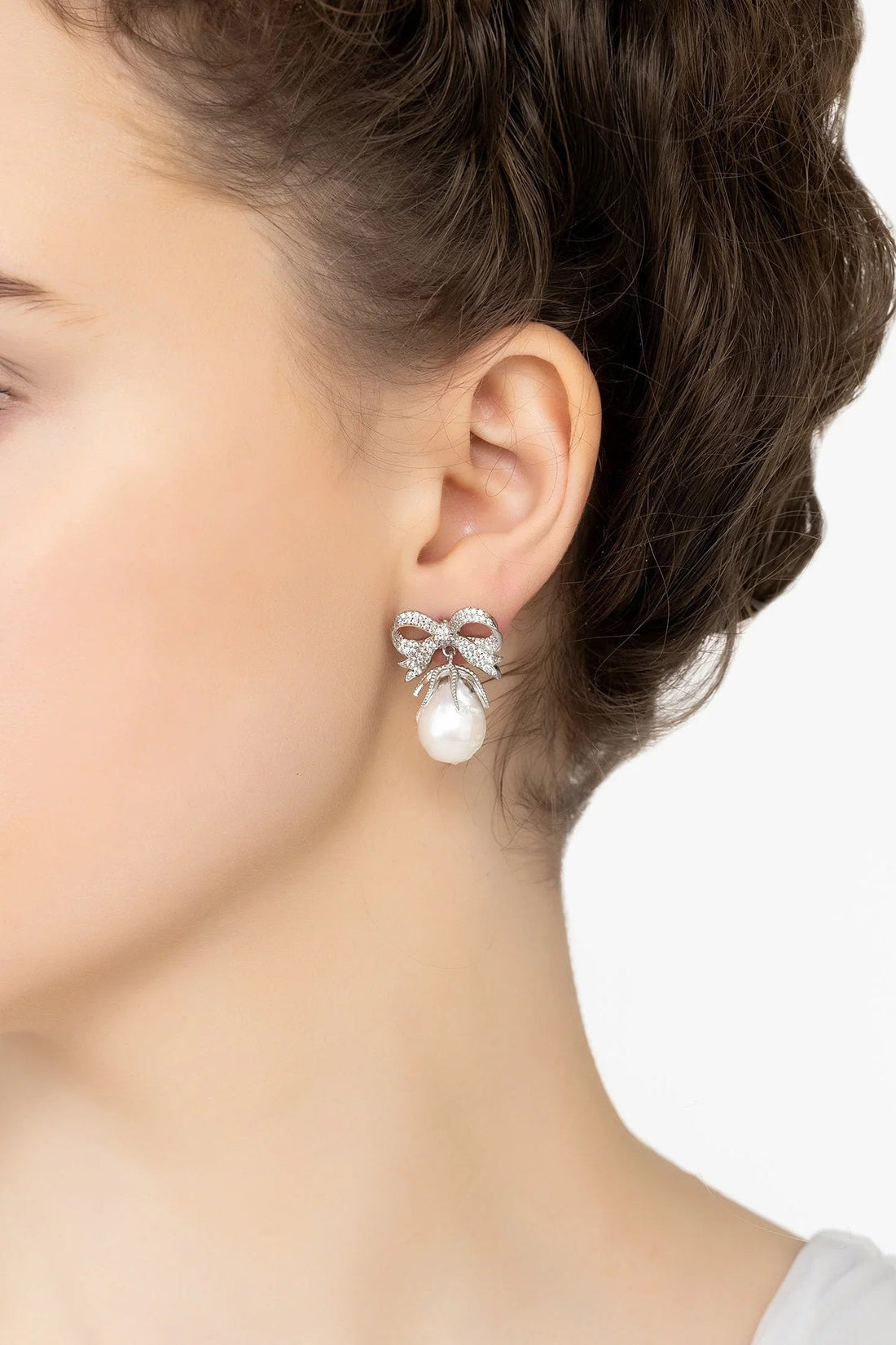 Silver pearl drop earrings with bow ribbon detail, worn close-up on ear
