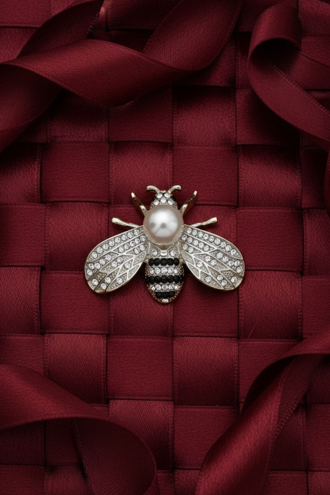 Silver-tone bee brooch with faux pearl and rhinestone accents on woven bag