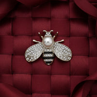Silver-tone bee brooch with faux pearl and rhinestone accents on woven bag