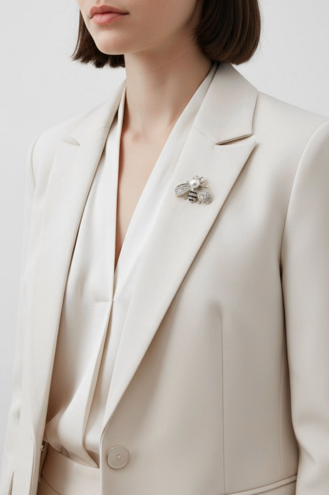 Bee brooch on light blazer lapel, faux pearl center with rhinestone wings