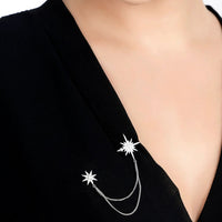 Silver starburst brooch with curved chain detail on a black dress