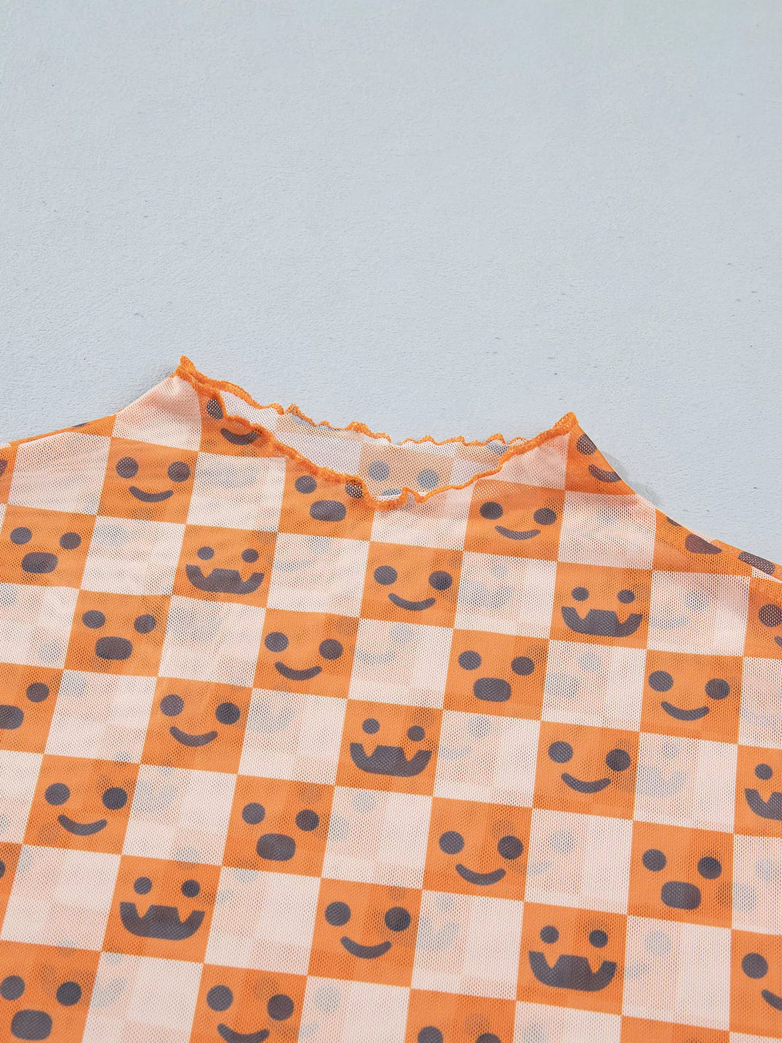 Close-up of orange-and-white checked fabric with smiling jack-o’-lantern faces and mock neck trim
