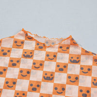Close-up of orange-and-white checked fabric with smiling jack-o’-lantern faces and mock neck trim