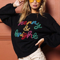 Black crewneck sweater with multicolor tinsel "Merry & bright" lettering, relaxed fit.