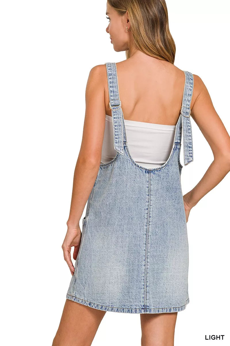 Back view of light wash denim overall dress with crisscross strap accents