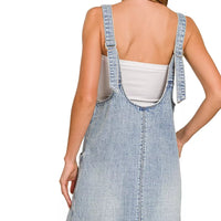 Back view of light wash denim overall dress with crisscross strap accents