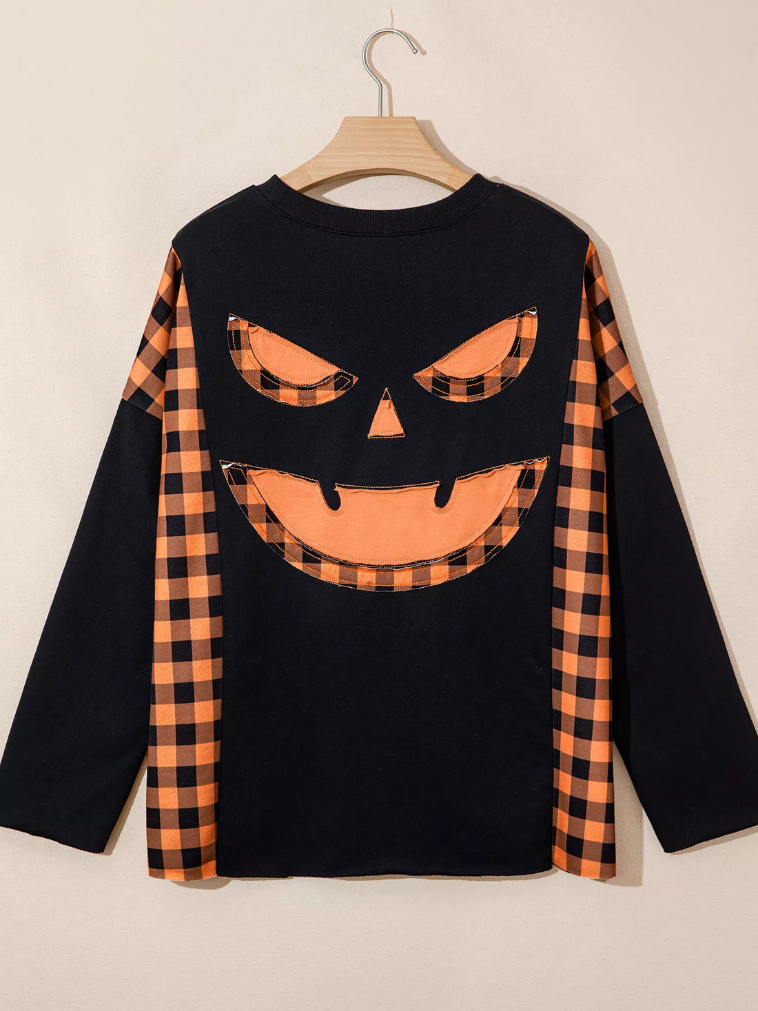 Black long-sleeve top with orange plaid pumpkin face graphic on front