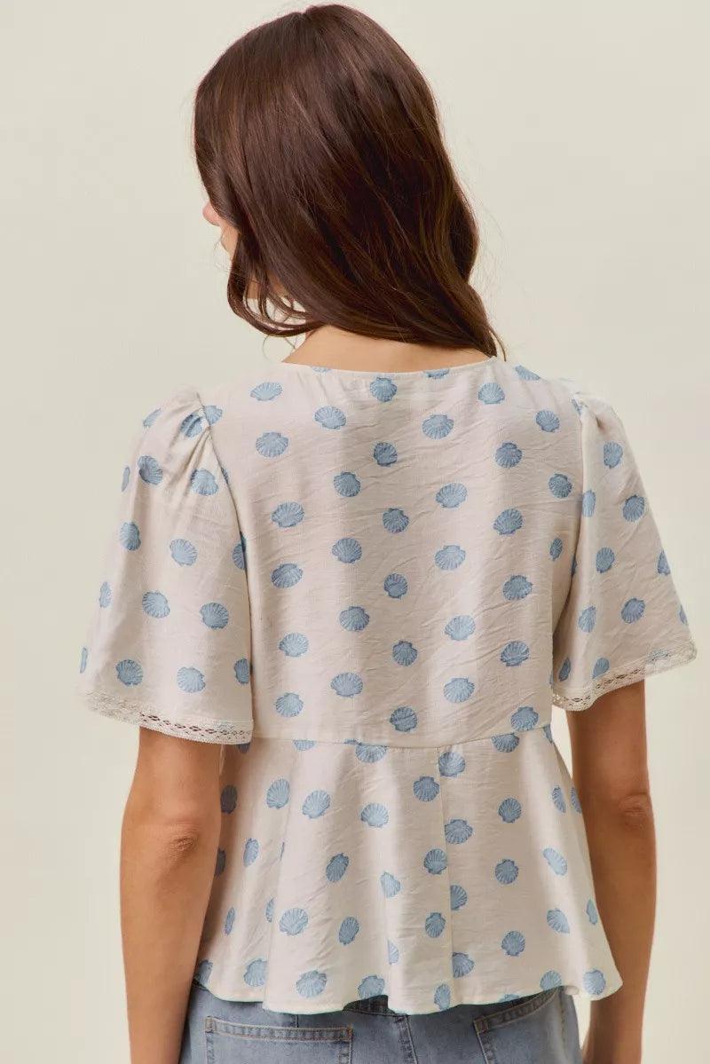 Back view of ivory dot-print blouse with gathered flutter sleeves and tiered waist.