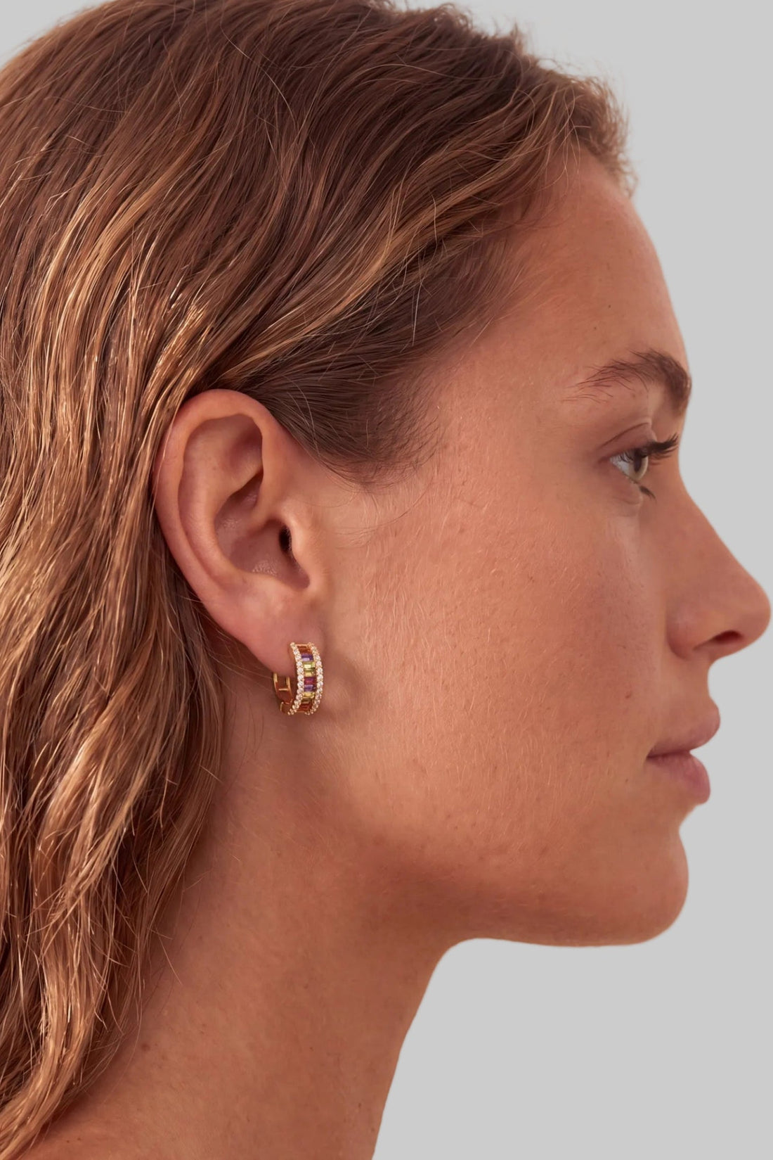 Gold-tone rainbow baguette huggie earrings on ear, shown in side profile