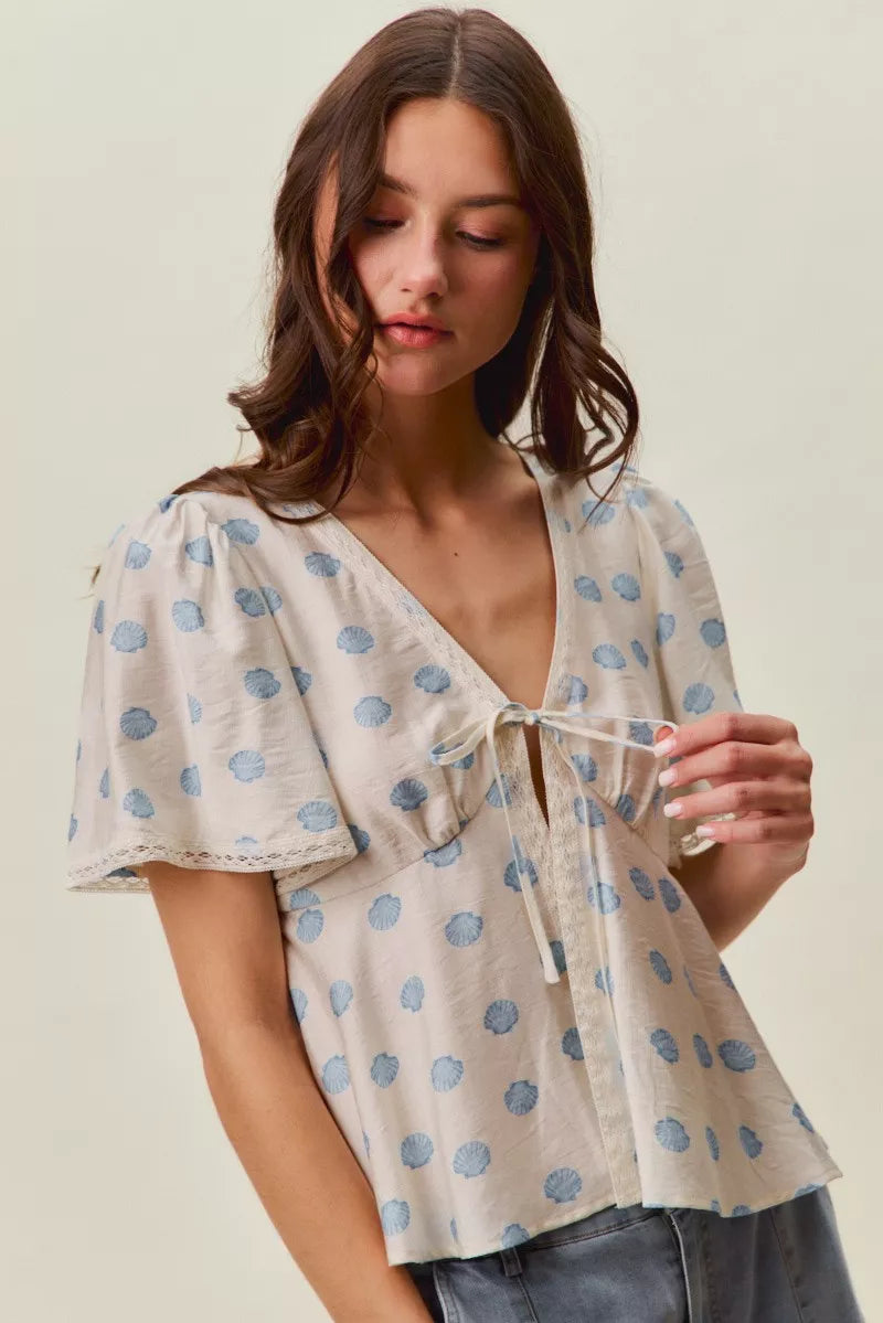 Ivory blouse with blue circular dot print, tie-front V-neck, and flutter sleeves.