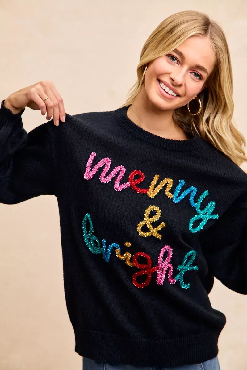 Black crewneck sweater with multicolor tinsel "Merry & bright" lettering, long sleeves.