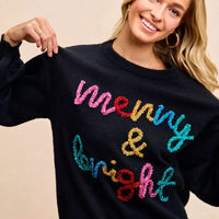 Black crewneck sweater with multicolor tinsel "Merry & bright" lettering, long sleeves.