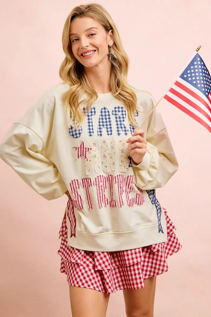 Cream sweatshirt with blue star lettering, red stripe graphic, and bow patch details.