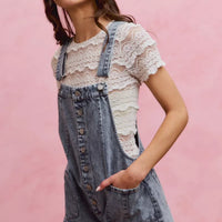 Light wash denim overall romper with adjustable straps and front buttons, wide leg shorts