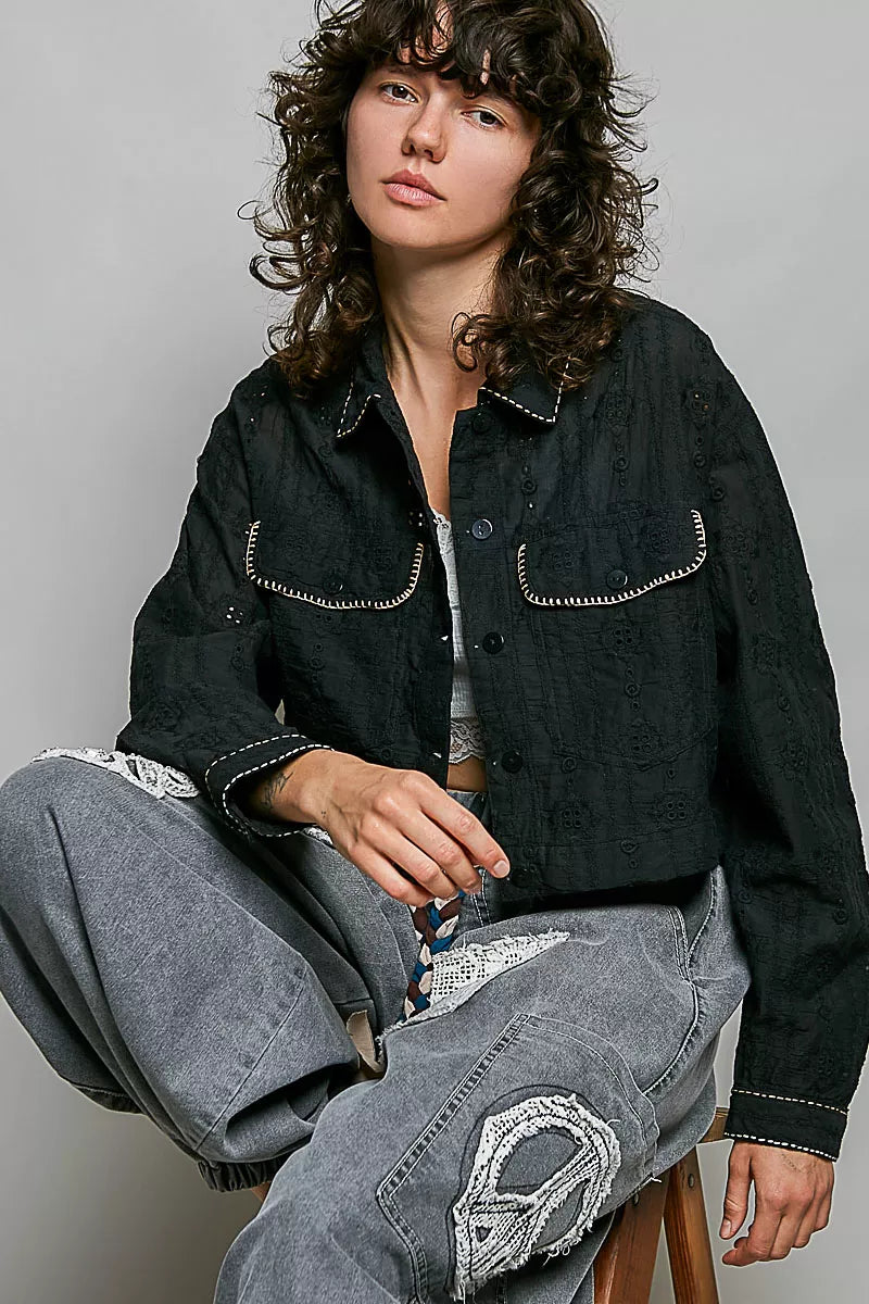 Black cropped button-front eyelet cotton jacket with scalloped pocket flaps and contrast trim.