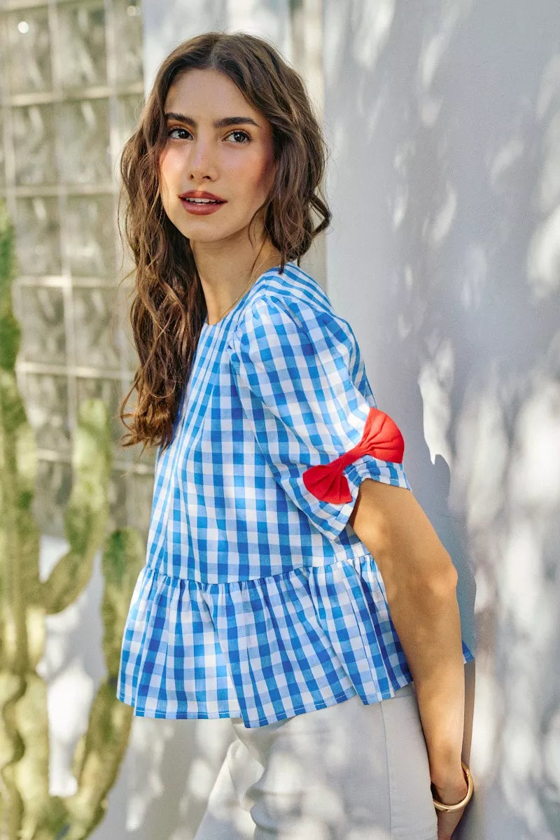 Blue gingham blouse with short puff sleeves and red ribbon bow accents at the cuff