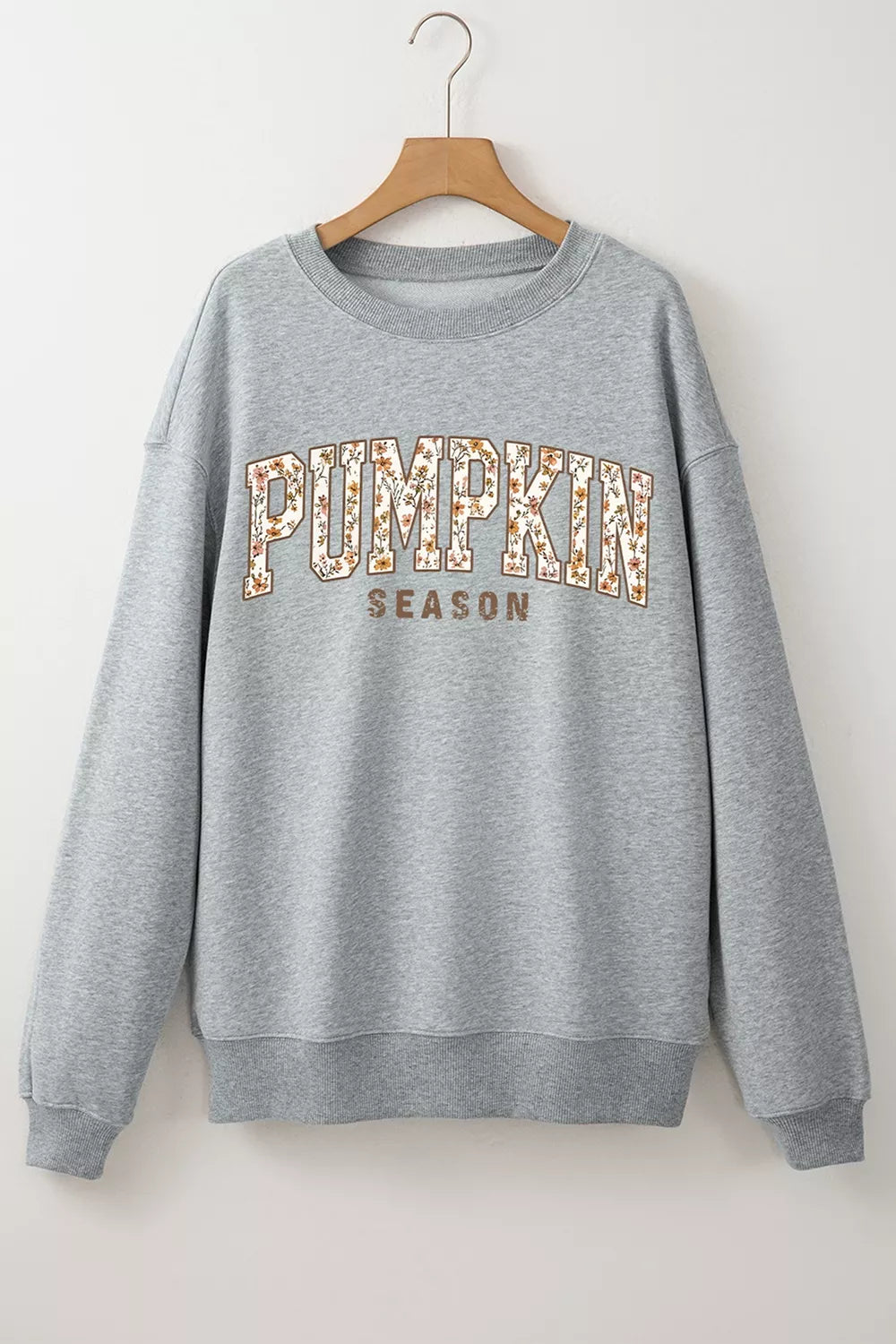 Gray oversized pullover sweatshirt hanging on a hanger, “PUMPKIN SEASON” chest graphic