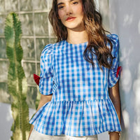 Blue gingham peplum blouse with flutter sleeves and red bow accents at the shoulders