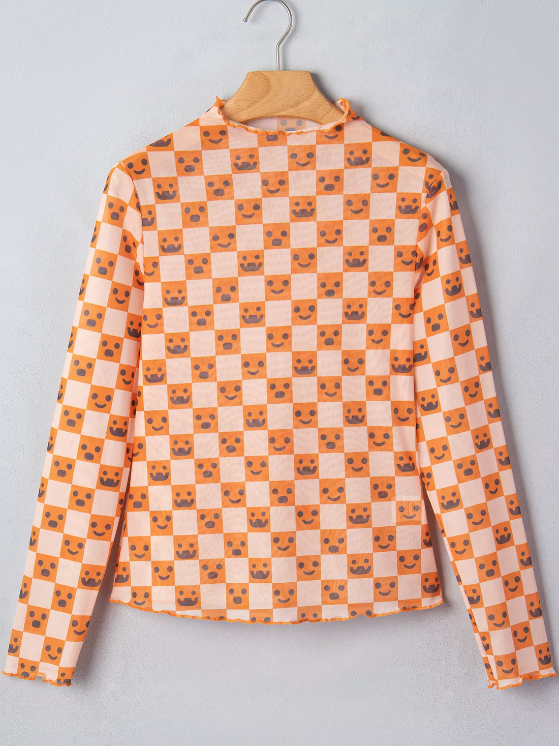 Orange-and-white Halloween blouse on hanger with mock neck, long sleeves, jack-o’-lantern checker print