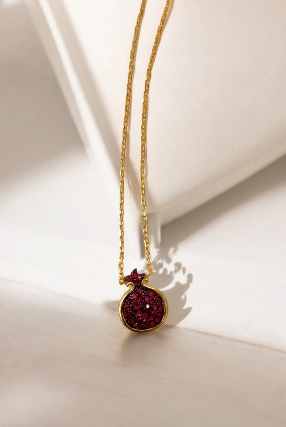 Gold pendant necklace with ruby-pink pomegranate charm in dark red crystal-set bezel