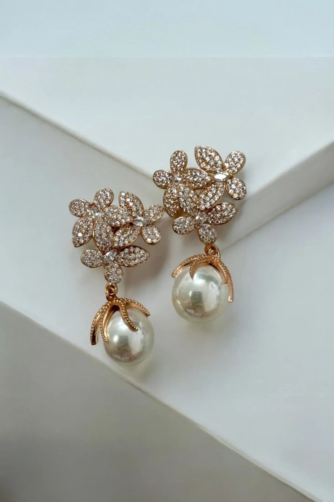 Gold rhinestone flower earrings with white pearl drop, angled close-up