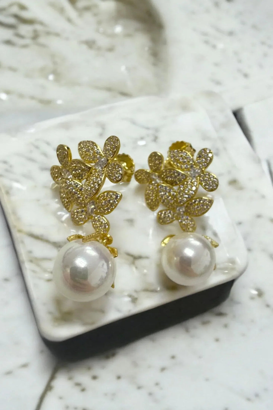 Gold rhinestone floral earrings with white pearl drops on jewelry tray