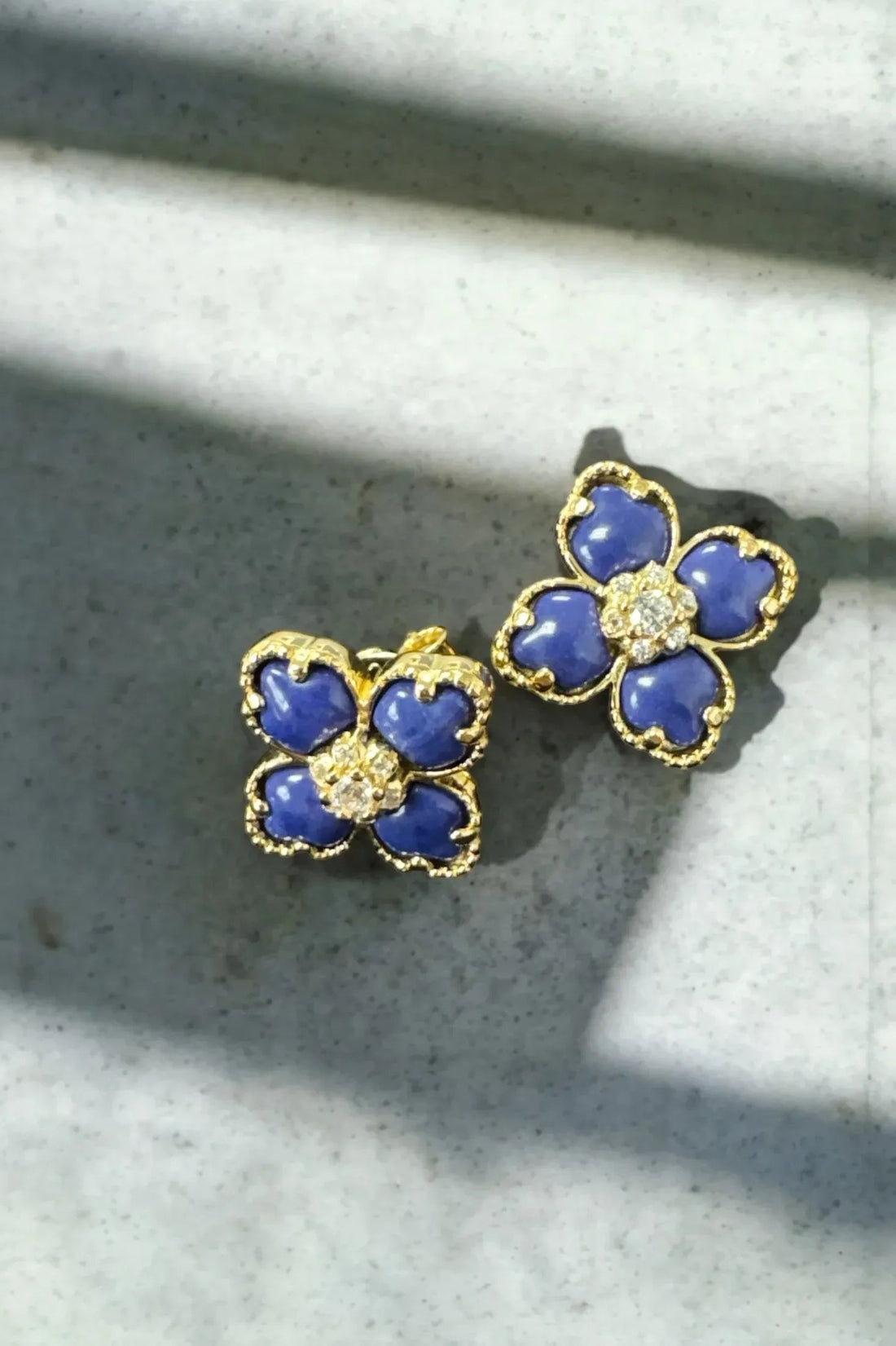 Close-up of gold-tone blue clover flower stud earrings with crystal centers