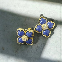 Close-up of gold-tone blue clover flower stud earrings with crystal centers