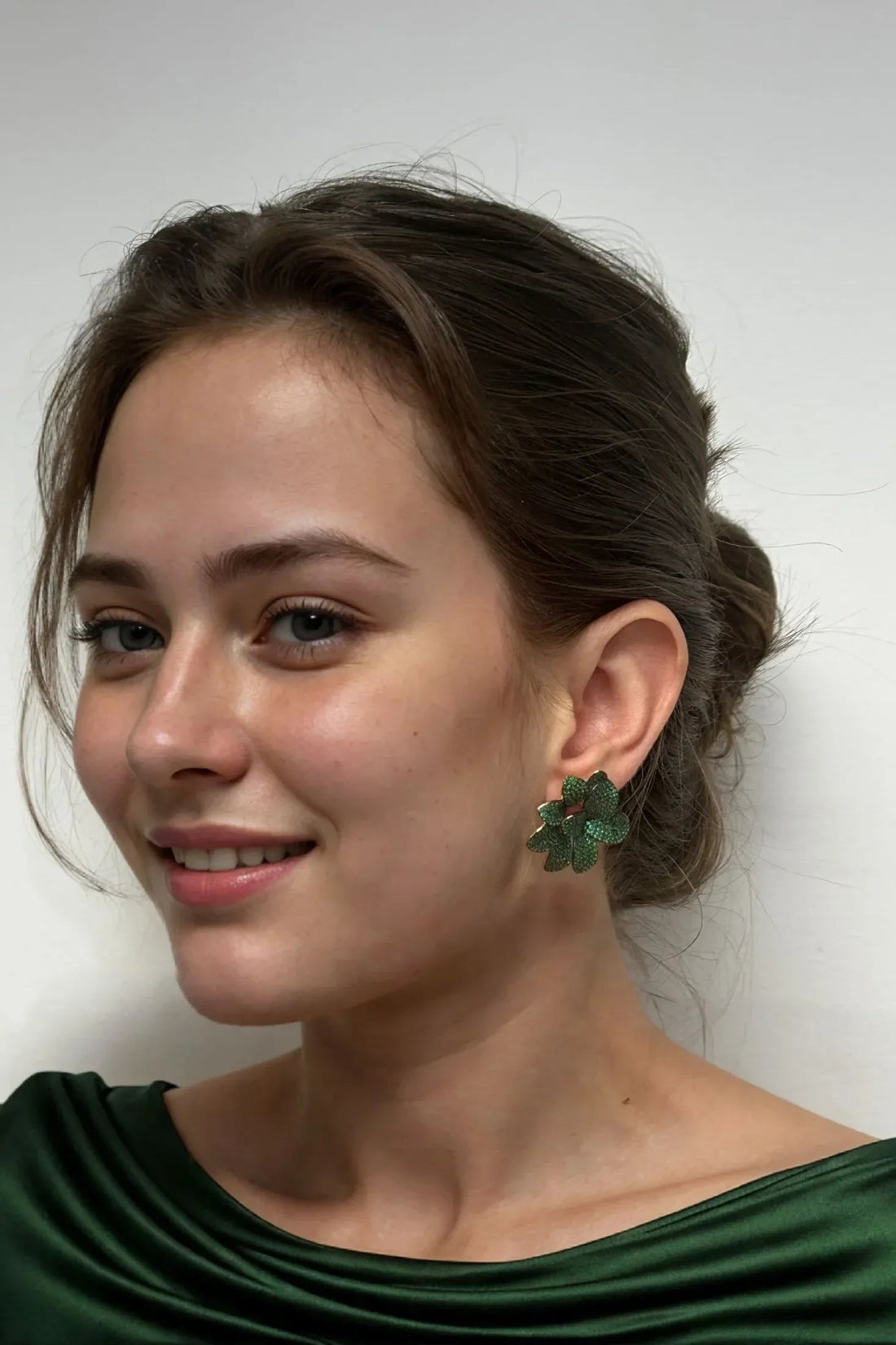 Large emerald-green flower stud earrings on model, gold-tone posts