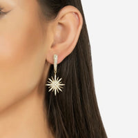 Gold starburst drop earrings on ear, featuring glittering sunburst charms on dangling stems