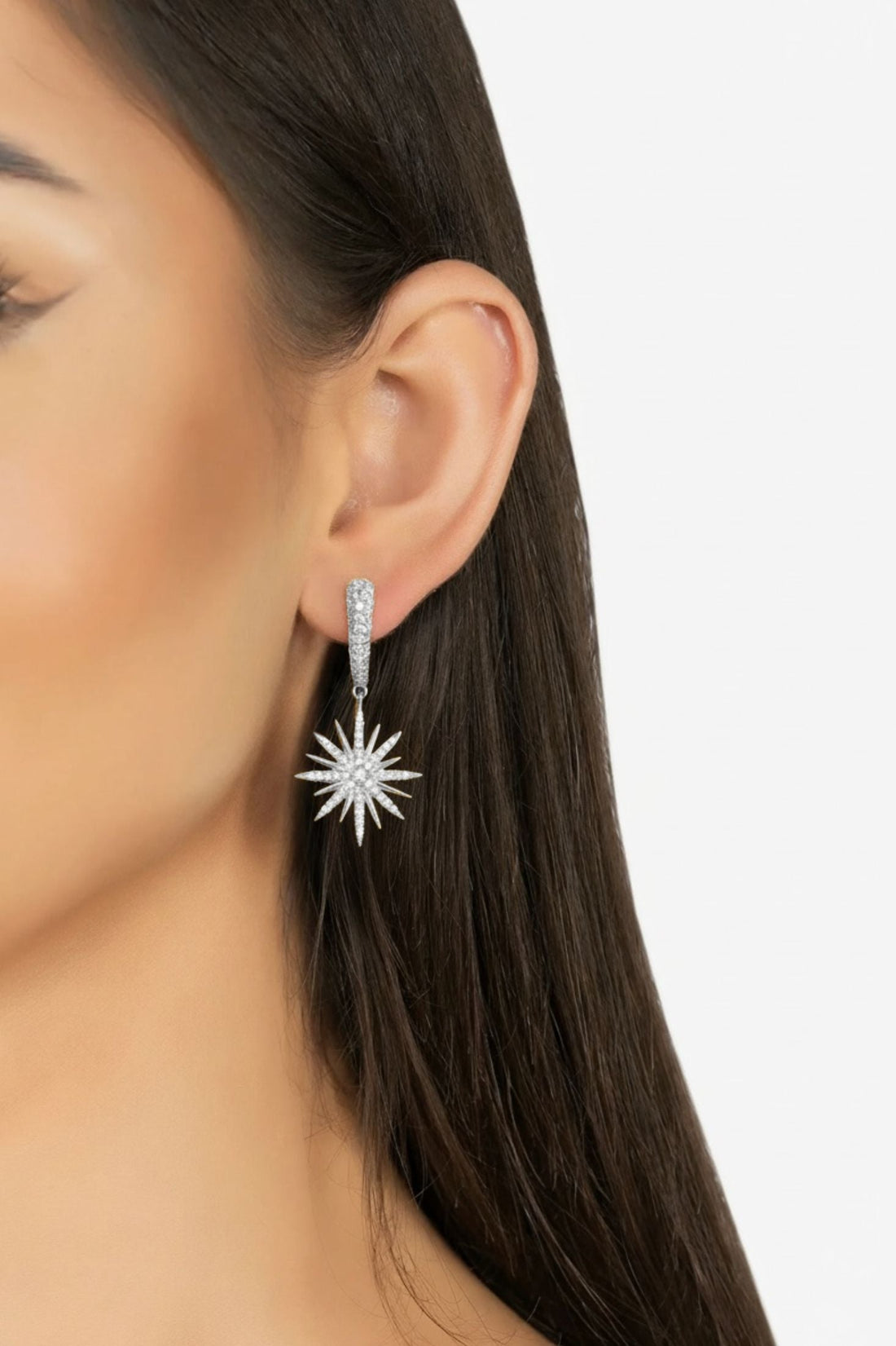 Silver starburst drop earrings on ear with a dangling sunburst charm