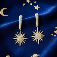 Pair of gold starburst drop earrings with crystal sunburst centers and slim dangling posts