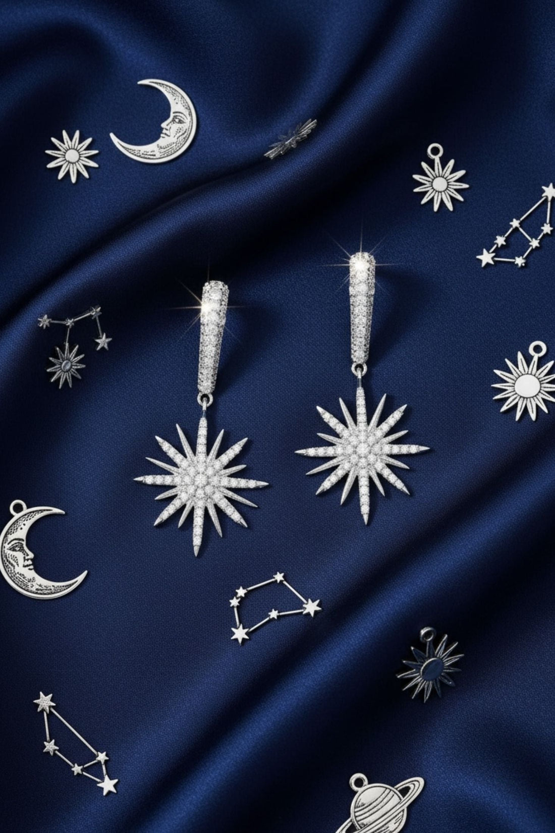 Silver starburst drop earrings with sunburst dangling charms shown on blue fabric