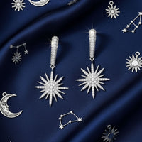 Silver starburst drop earrings with sunburst dangling charms shown on blue fabric